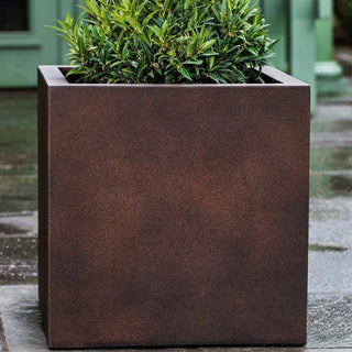 A square, dark brown planter with a small shrub, placed outdoors.