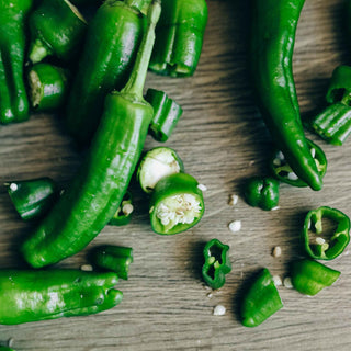 Fresh green chili peppers, some whole and some sliced, on a wooden surface.