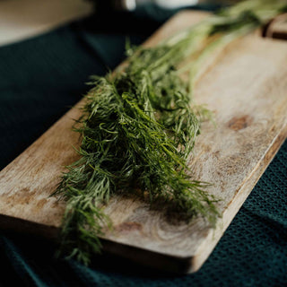 Fresh dill on a wooden cutting board, showcasing its vibrant green fronds and ready for culinary use.