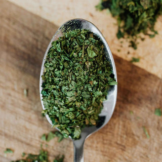 A close-up of dried herbs on a spoon placed on a wooden surface.